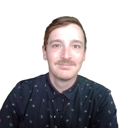 A man with a mustache wearing a dark patterned button-up shirt, photographed against a plain white background.
