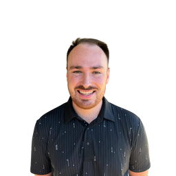 A smiling man with short brown hair and a light beard, wearing a dark navy short-sleeve button-up shirt with a subtle white vertical stripe pattern, set against a solid white background.