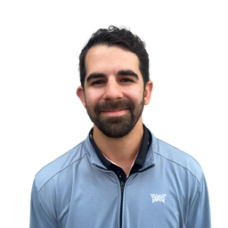 A man with dark hair and a beard wearing a light blue athletic zip-up jacket with a white logo on the left chest, set against a plain white background.