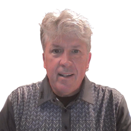 A man with short, wavy gray hair wearing a gray and black patterned knit vest over a dark collared shirt, shown against a plain white background.