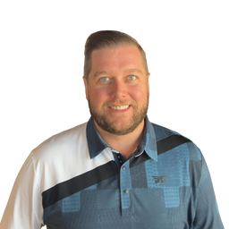 A smiling man with short brown hair and a beard wearing a blue and white patterned polo shirt with a black diagonal stripe, photographed against a plain white background.