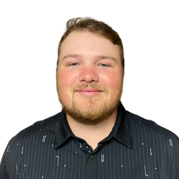 A man with short brown hair and a light beard wearing a black button-down shirt with a subtle white vertical stripe pattern, photographed against a solid white background.
