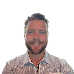 A smiling man with short brown hair and a beard, wearing a small checkered button-up shirt, photographed against a plain white background.