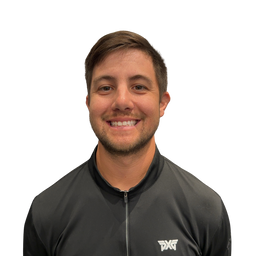 A smiling man with short brown hair and light stubble, wearing a black athletic zip-up jacket with a white logo on the left chest, photographed against a plain white background.