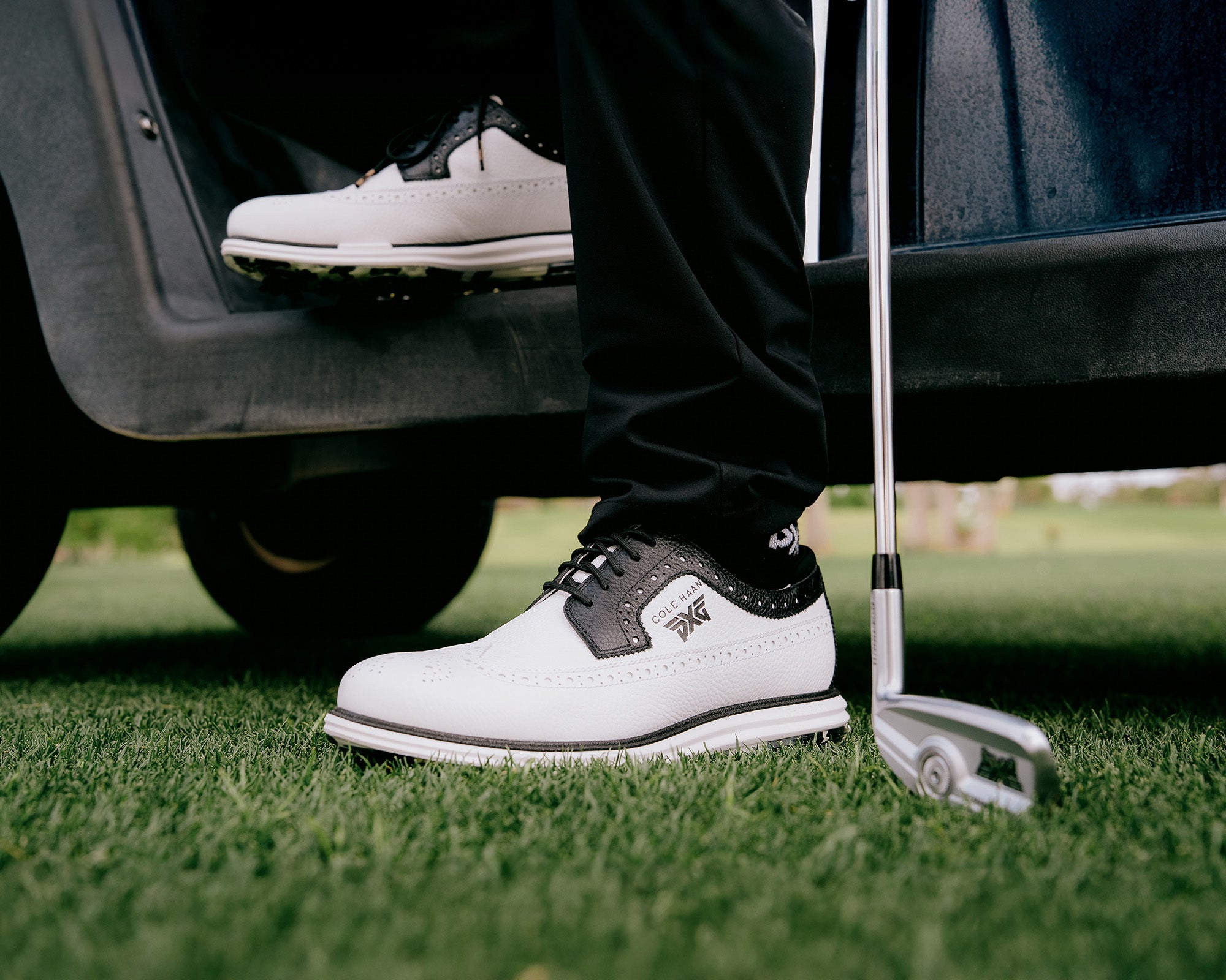 Golf shoes on a golf course with a golf club nearby