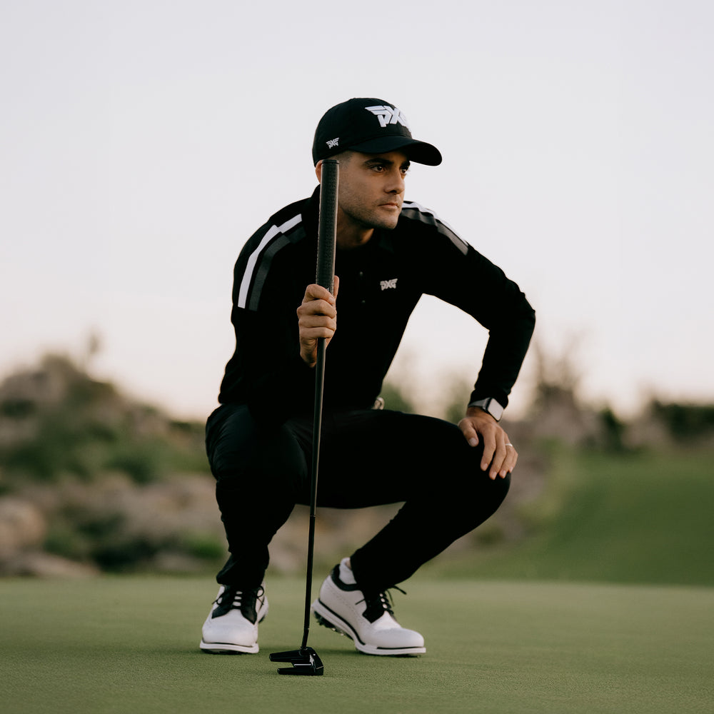 Golfer in black outfit and cap on a golf course