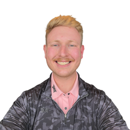 A smiling man with blond hair and a mustache wearing a dark gray camouflage zip-up jacket over a light pink polo shirt, photographed against a plain white background.