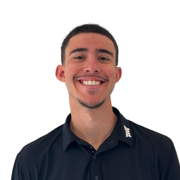 A smiling young man with short dark hair and a light beard, wearing a black collared button-up shirt with a white logo on the left shoulder, photographed against a plain white background.