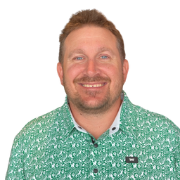 A smiling man with short brown hair and a light beard wearing a green and white patterned button-down shirt, photographed against a plain white background.