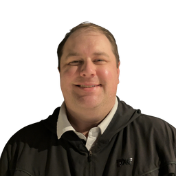 A man smiling, wearing a black zip-up hoodie over a white collared shirt, isolated on a white background.