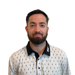 A man with a beard and short dark hair wearing a white button-up shirt with a black pattern and a black collar, photographed against a plain white background.