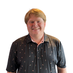 A smiling man with blond hair wearing a dark patterned short-sleeve polo shirt over a light pink collared undershirt, photographed against a plain white background.