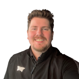A smiling man with short brown hair and a beard wearing a black zip-up jacket with a white logo on the left chest, photographed against a plain white background.