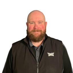 A bald man with a full brown beard wearing a black zip-up vest with a white DXG logo on the left chest, over a dark gray collared shirt, against a plain white background.