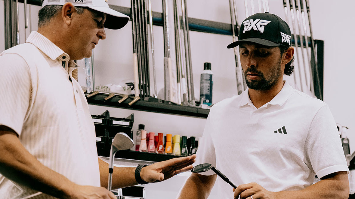 Two men in golf apparel standing indoors in a shop or studio, one wearing a white PXG cap and polo and the other wearing a black PXG cap and white Adidas polo. Golf clubs and accessories are visible in the background.