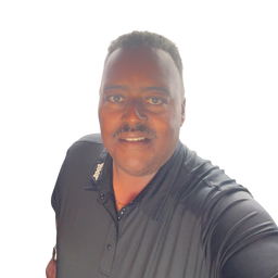 A man wearing a dark gray short-sleeve polo shirt, captured in a selfie-style portrait against a bright white background.
