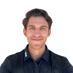 A man with short brown hair smiling, wearing a black button-down shirt with a small white logo on the collar, set against a plain white background.