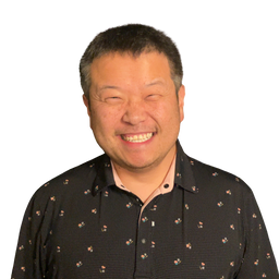 A smiling man with short dark hair wearing a black button-down shirt with a small floral pattern, photographed against a plain white background.
