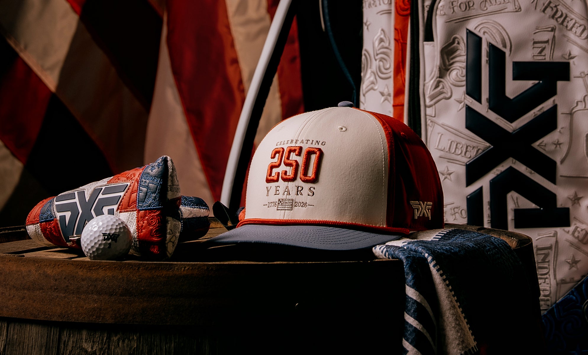 Baseball cap with '250 Years' text, golf balls, and towel on a wooden surface with decorative background
