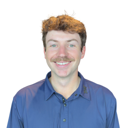A smiling man with curly light brown hair and a mustache wearing a blue button-up shirt, photographed against a plain white background.