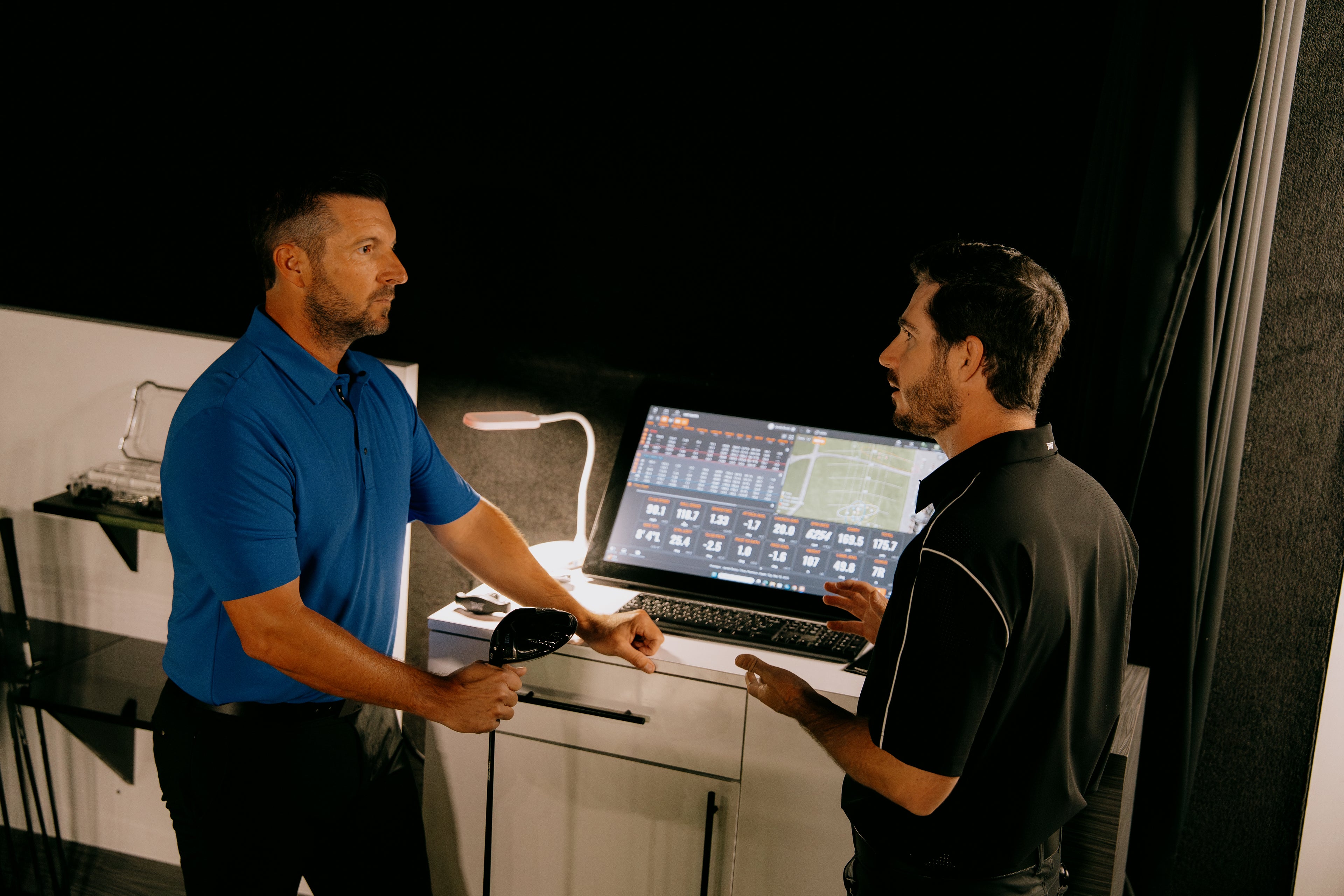Two men discussing a laptop displaying software on a dark background