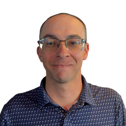 A man with short brown hair and glasses, wearing a navy blue patterned button-down shirt, shown against a solid white background.