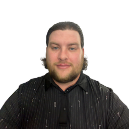 A man with a beard and slicked-back hair wearing a black button-down shirt with a subtle white vertical stripe pattern, photographed against a solid white background.