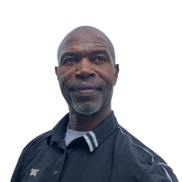 A man with a shaved head and gray beard wearing a black collared athletic jacket with white stripes on the collar, photographed against a plain white background.