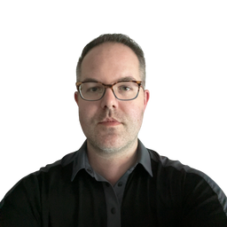 A man with short dark hair and glasses, wearing a black button-up shirt over a dark gray collared shirt, photographed against a plain white background.