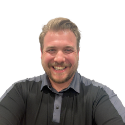 A smiling man with blond hair and a short beard, wearing a dark gray long-sleeve polo shirt with lighter gray shoulder panels, set against a plain white background.