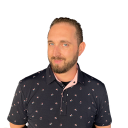 A man with a beard and short brown hair wearing a dark navy patterned polo shirt with a pink inner collar, photographed against a solid white background.