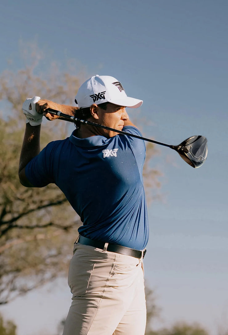 Golfer in blue shirt and white cap swinging a golf club with a clear sky background