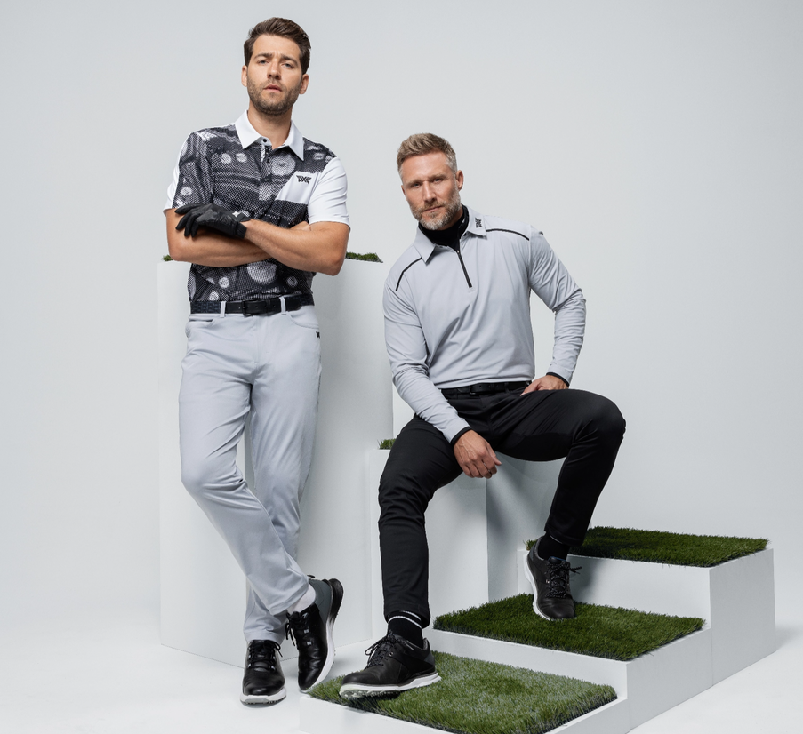 Two men in new golf apparel for fall '23, sitting on cubes.
